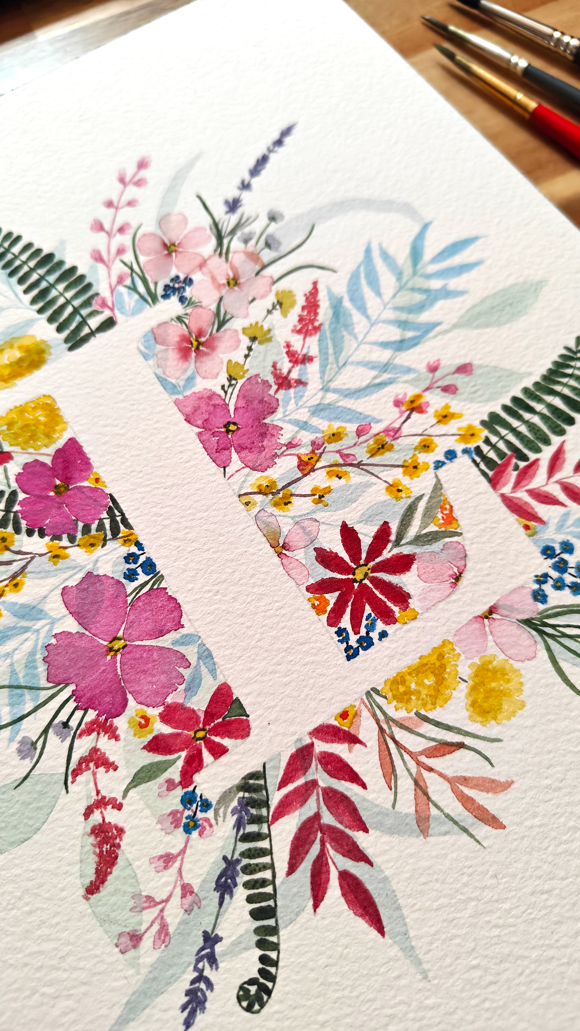 Closeup detail of loral design on a white background surrounding white L, with paintbrushes in the corner. Made with watercolours.