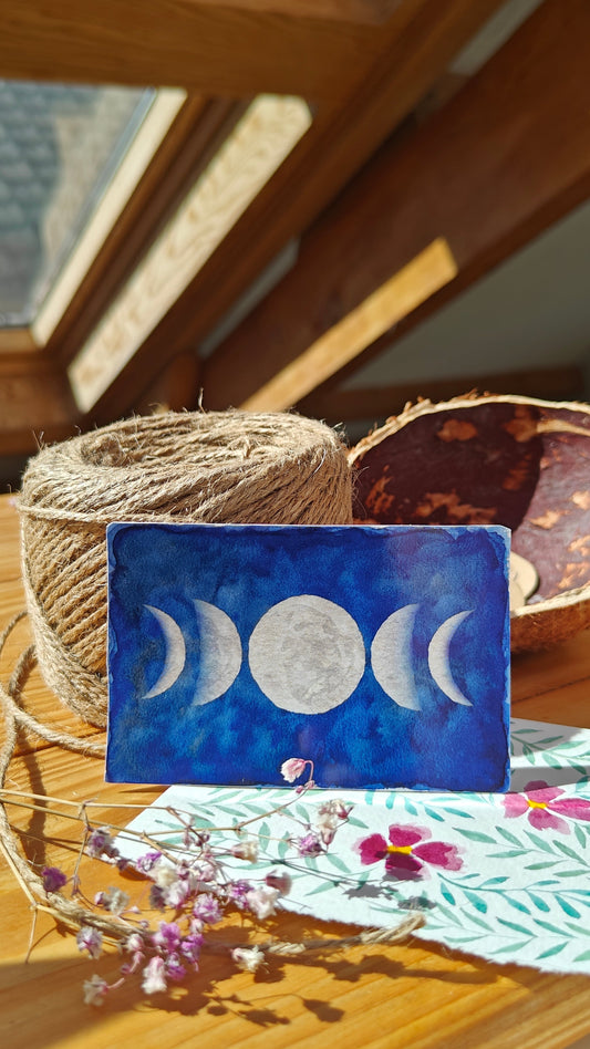 Sticker with moon phases over a wooden surface with twine, watercolour painting and flowers.