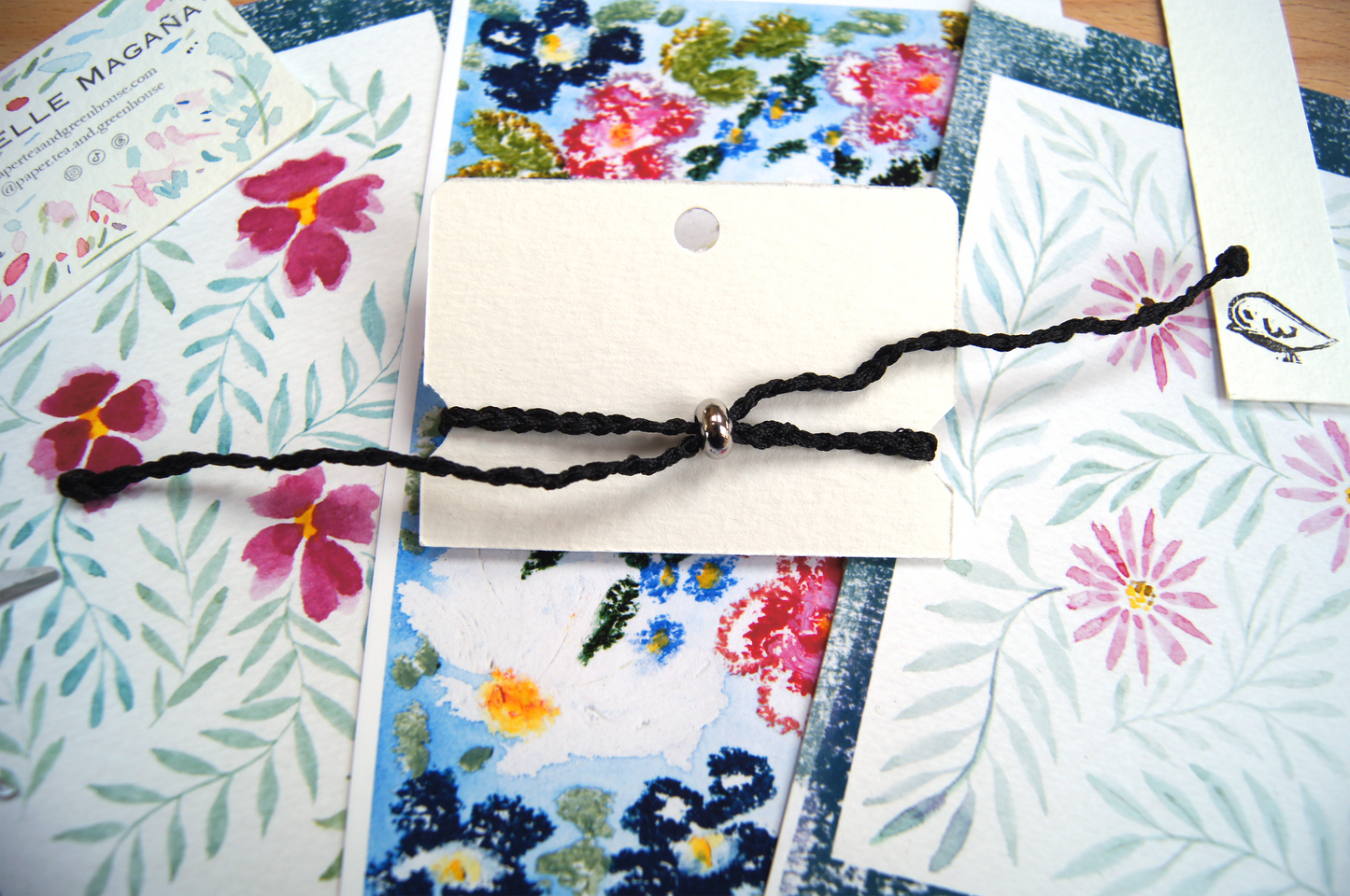Back of bracelet with adjustable bead, in its original package with a background floral watercolour paintings.