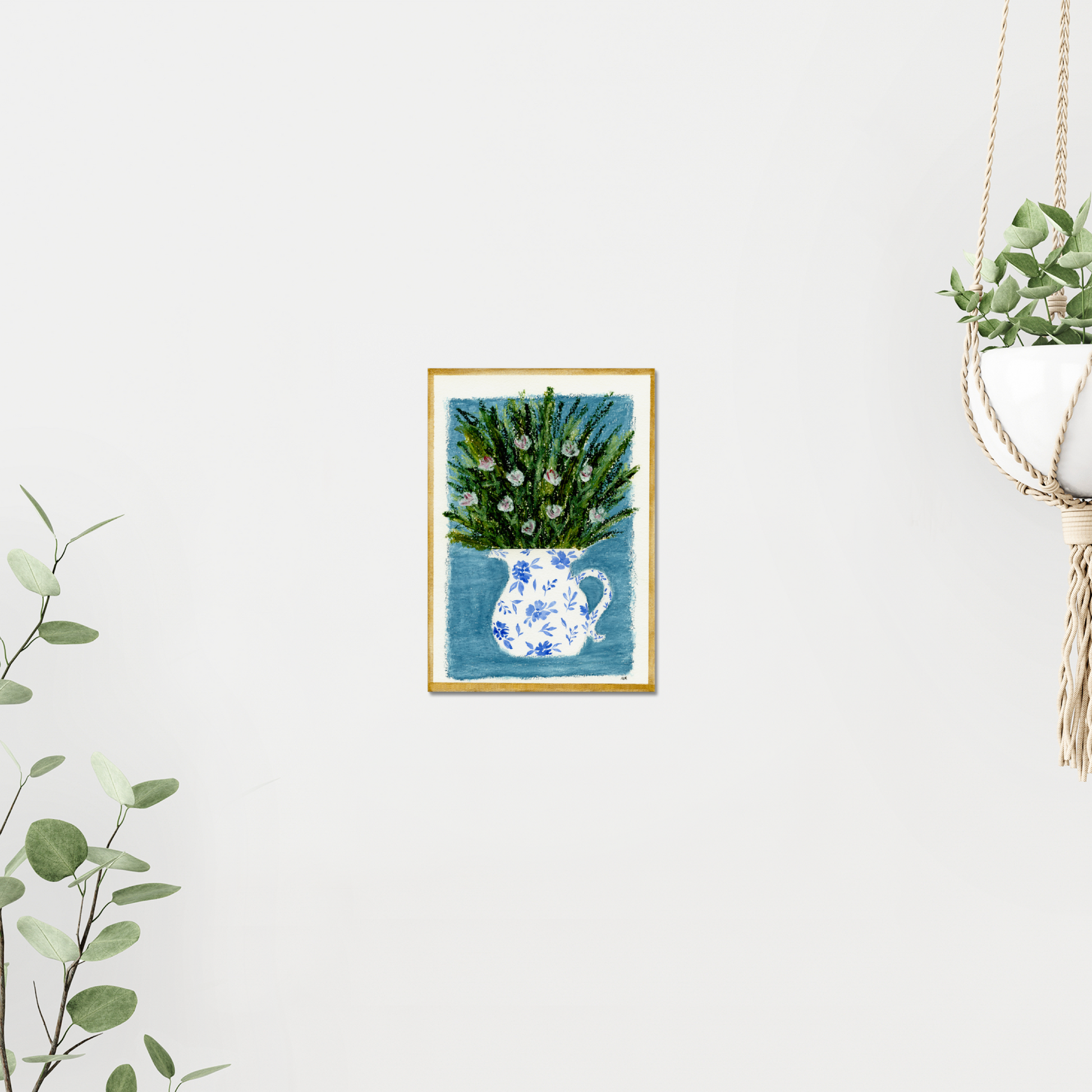 Framed artwork of a floral arrangement in a blue and white pitcher on a light blue background and a gold frame. On a white wall surrounded by plants. Made with oil pastels.
