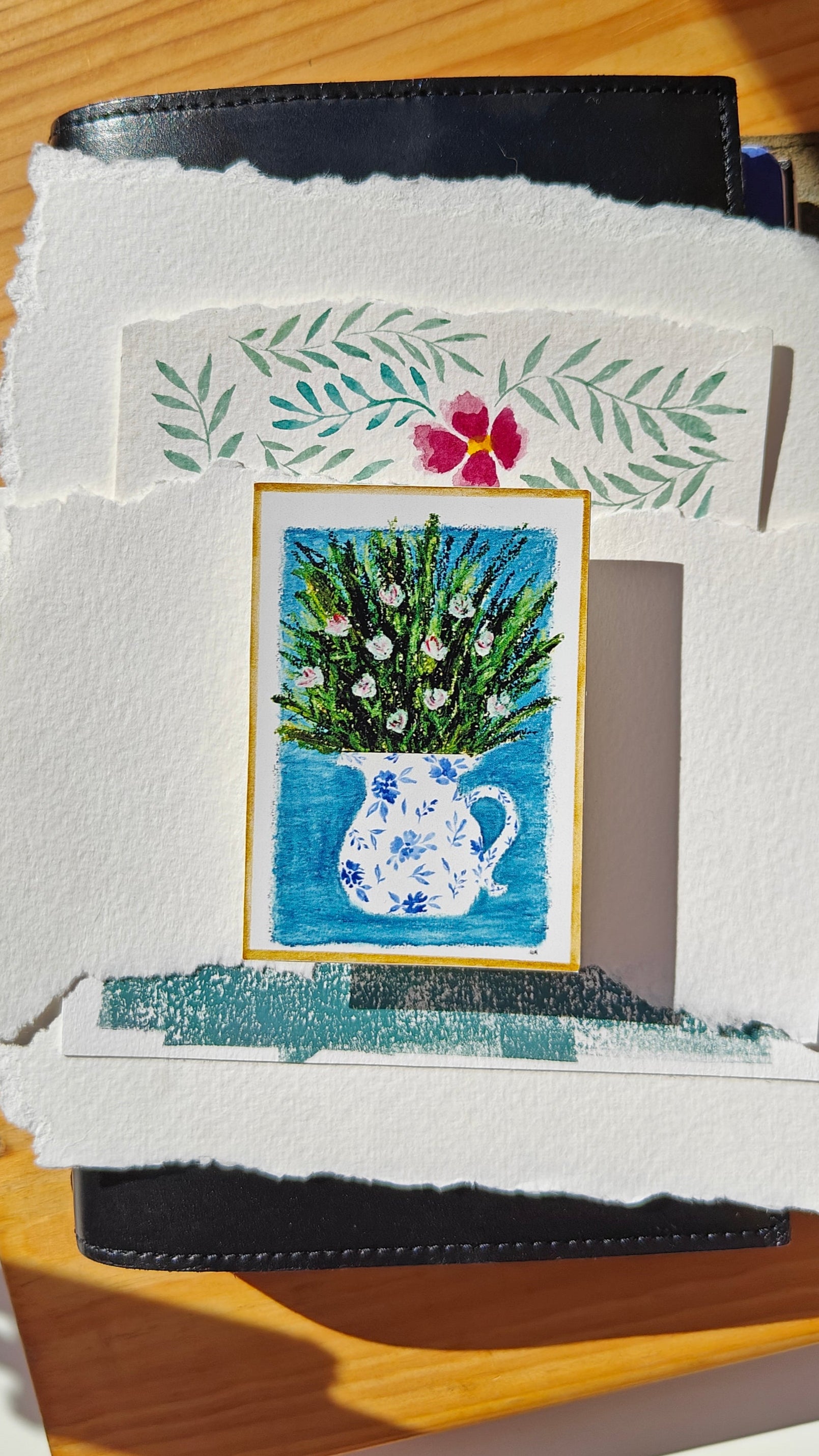 Sticker of an oil pastel and watercolour painting of a decorated, white pitcher with flowers and greenery, over various cuttings of paper and a leather journal