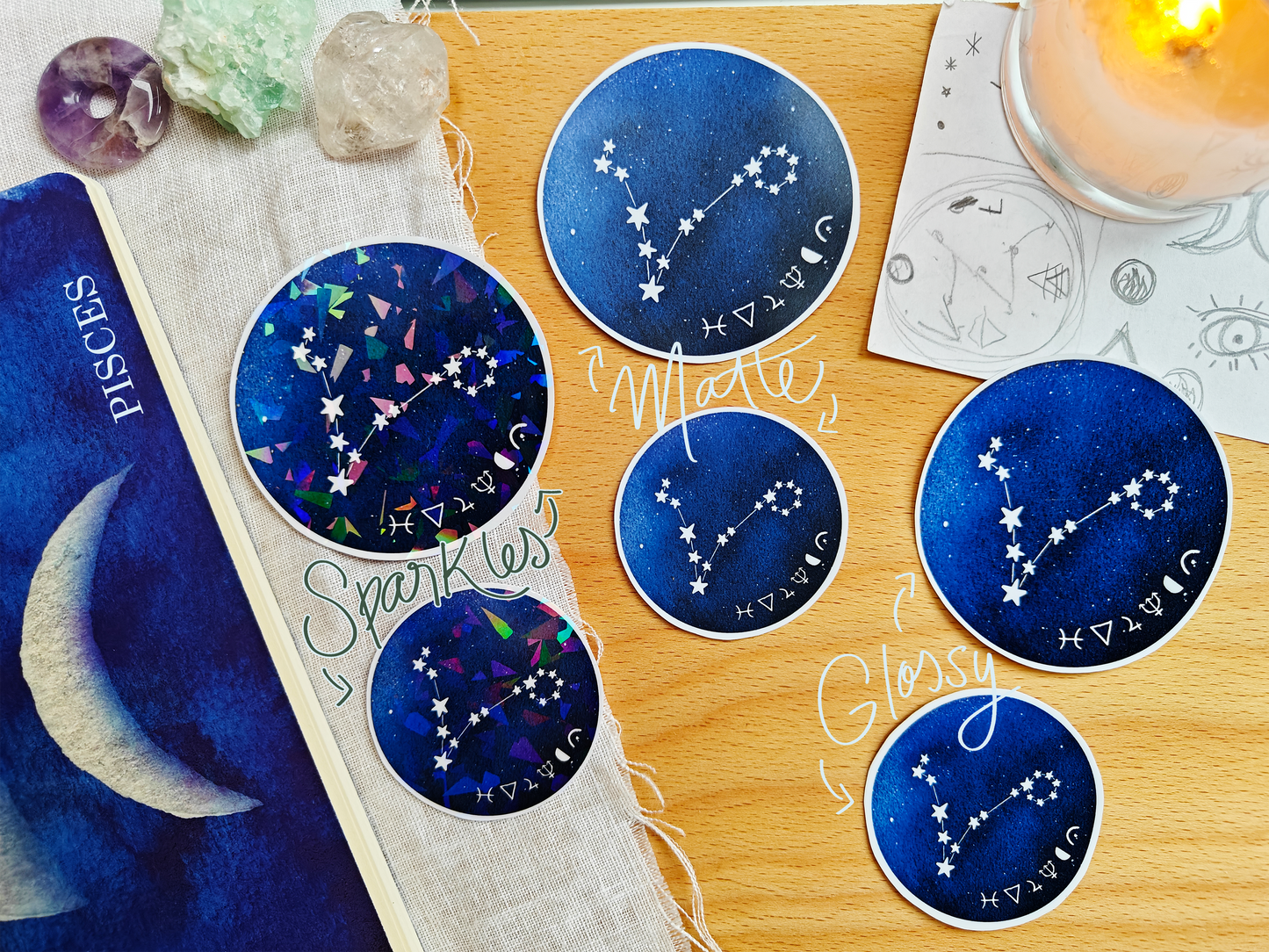 Set of blue astrological Constellation Stickers on a wooden surface with a candle, a journal, sketches, tarot cards and crystals.