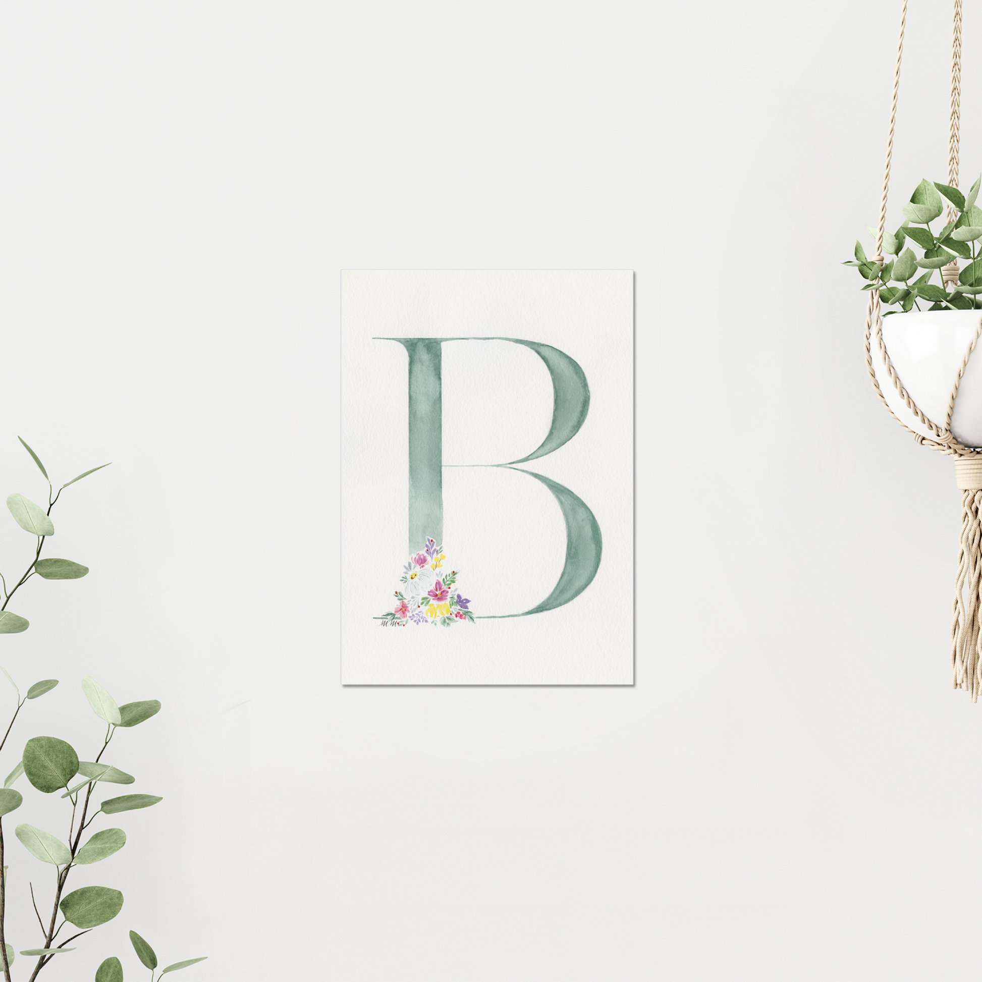 Letter 'B' print with floral design on a white wall, surrounded by greenery. Made with watercolours.