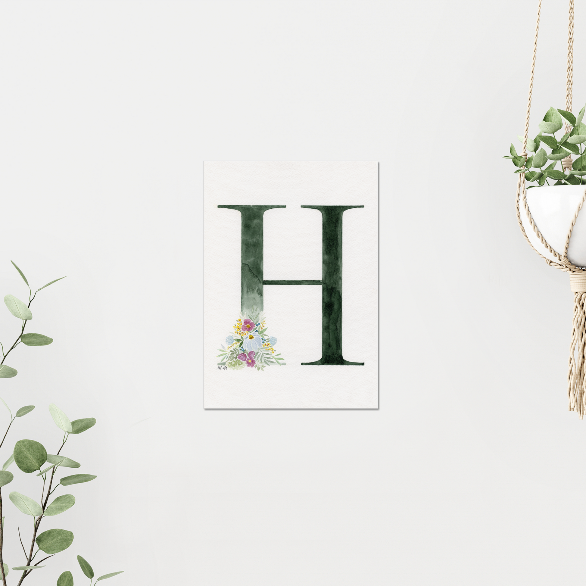 Letter 'H' print with floral design on a white background. On a white wall, surrounded by plants. Made with watercolours.