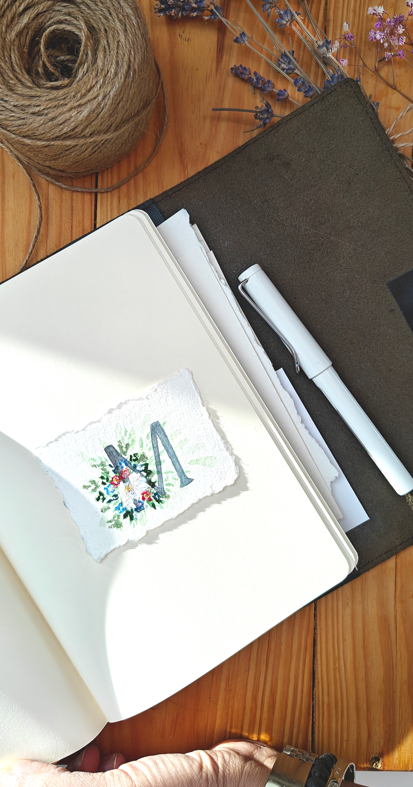 Open notebook with pen, twine, and dried flowers and lavender on a wooden surface