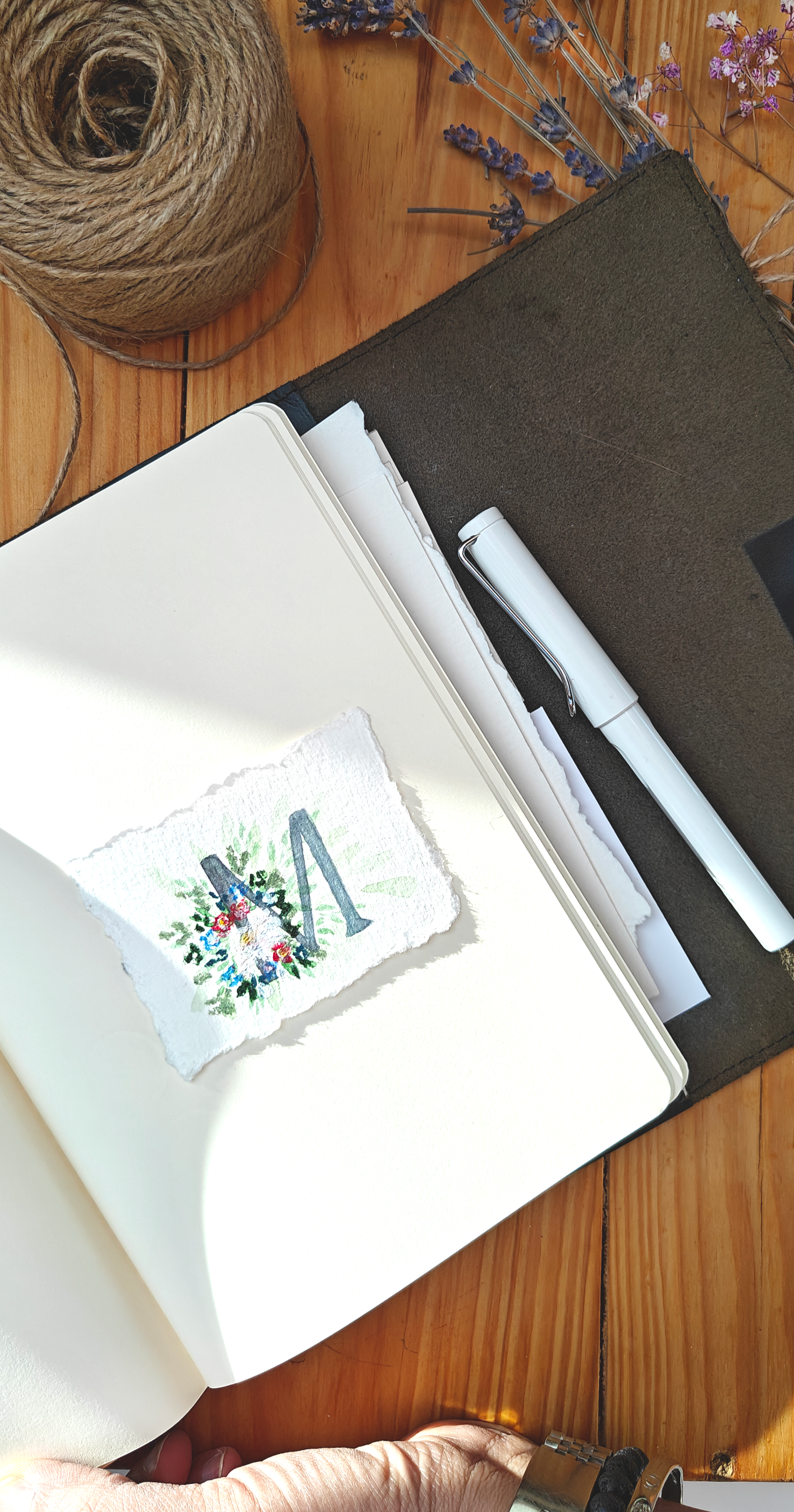Open notebook with pen, twine, and dried flowers and lavender on a wooden surface