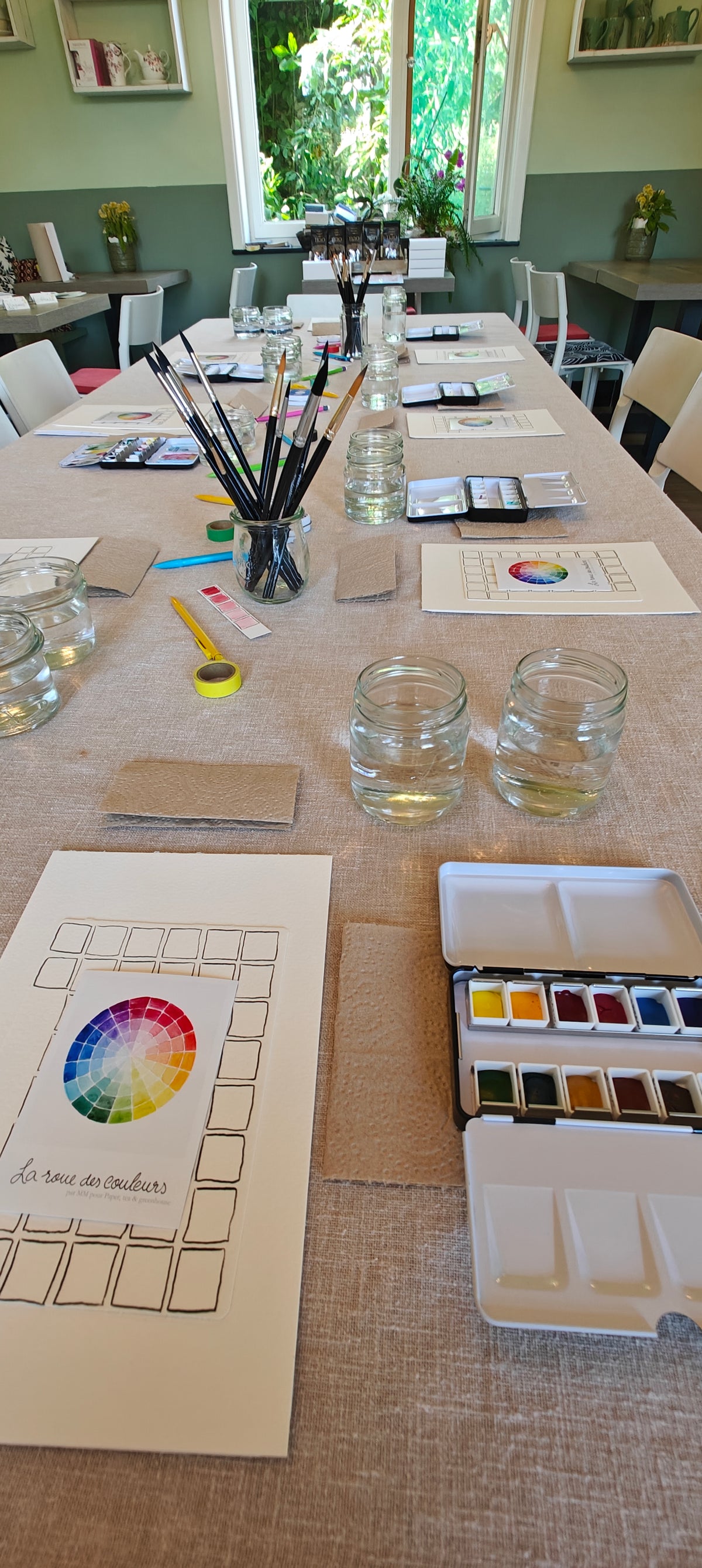 Artistic setup with watercolor supplies on a table, including color charts and brushes.