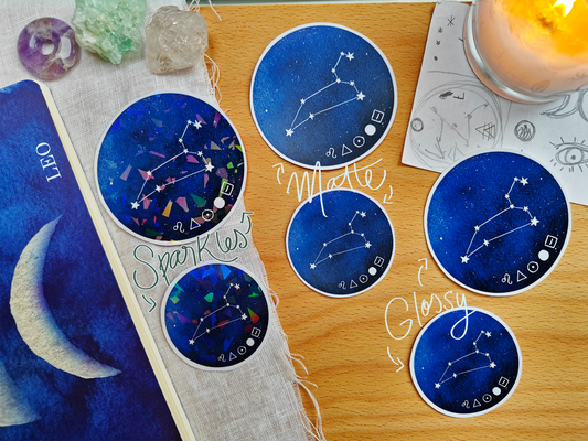 Set of blue celestial Constellation Stickers on a wooden surface with a candle, a journal, sketches, tarot cards and crystals.