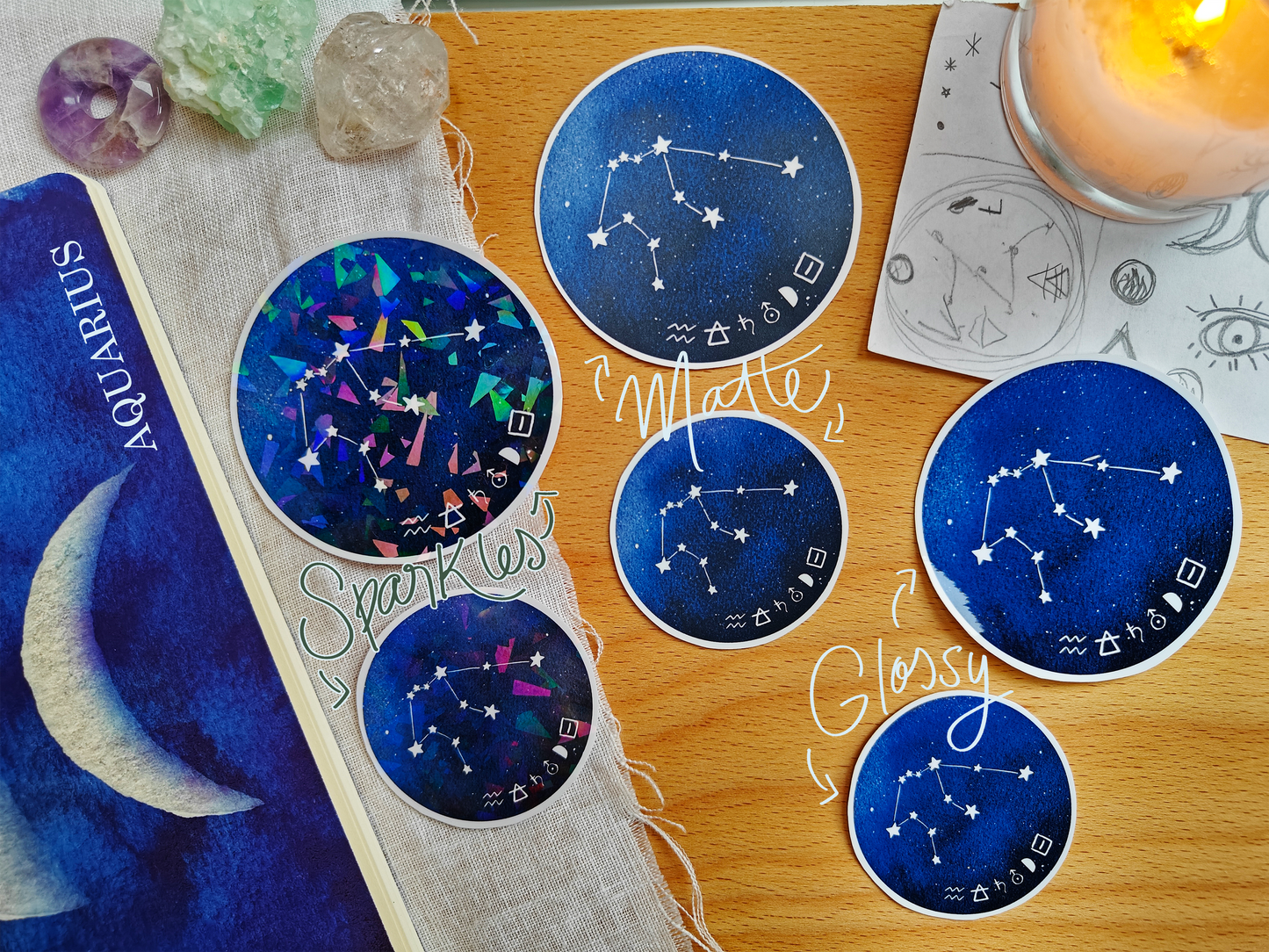 Set of blue astrological Constellation Stickers on a wooden surface with a candle, a journal, sketches, tarot cards and crystals.
