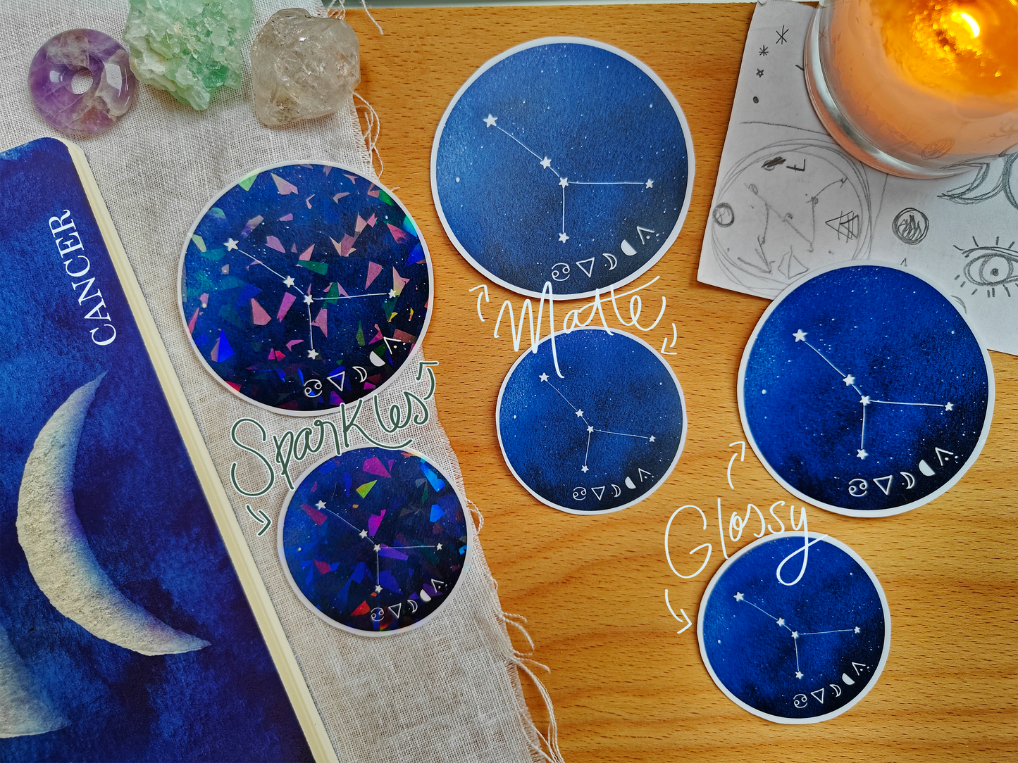 Set of blue astrological Constellation Stickers on a wooden surface with a candle, a journal, sketches, tarot cards and crystals.