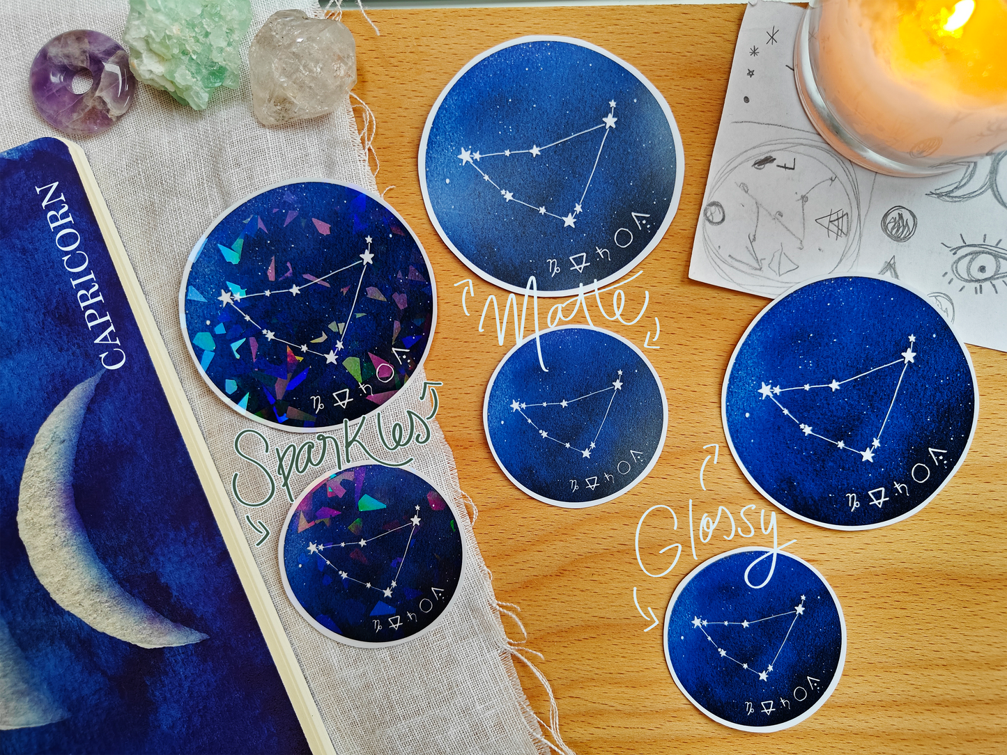 Set of blue astrological Constellation Stickers on a wooden surface with a candle, a journal, sketches, tarot cards and crystals.