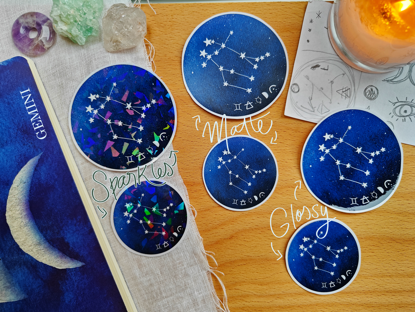 Set of blue astrological Constellation Stickers on a wooden surface with a candle, a journal, sketches, tarot cards and crystals.