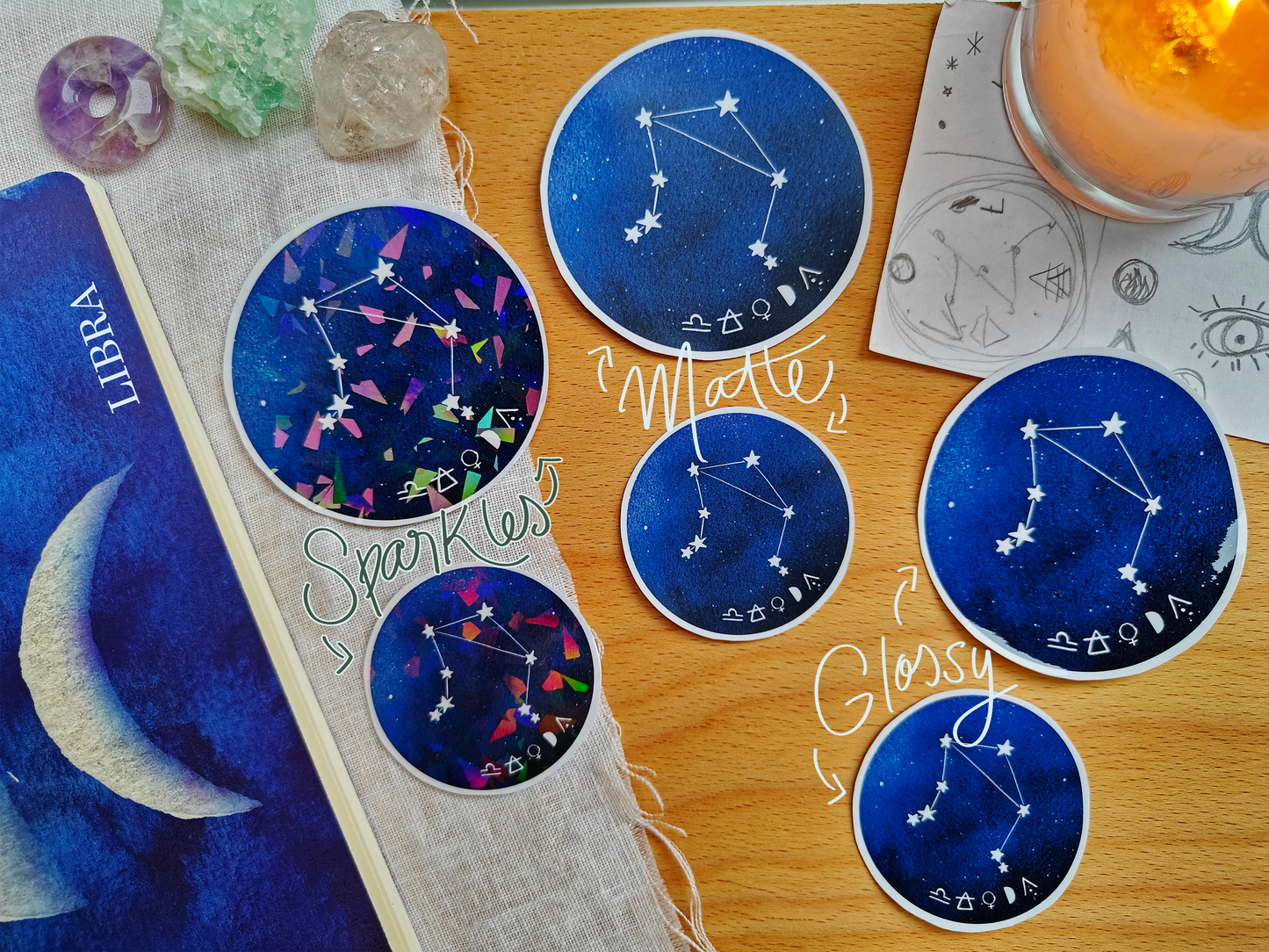 Set of blue astrological Constellation Stickers on a wooden surface with a candle, a journal, sketches, tarot cards and crystals.