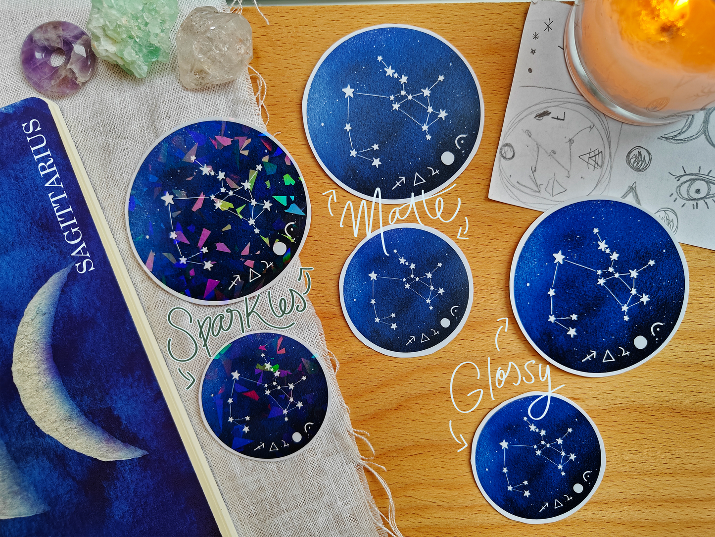 Set of blue astrological Constellation Stickers on a wooden surface with a candle, a journal, sketches, tarot cards and crystals.