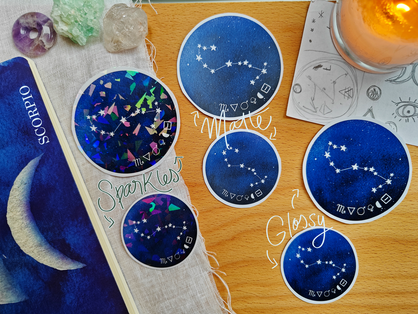 Set of blue astrological Constellation Stickers on a wooden surface with a candle, a journal, sketches, tarot cards and crystals.