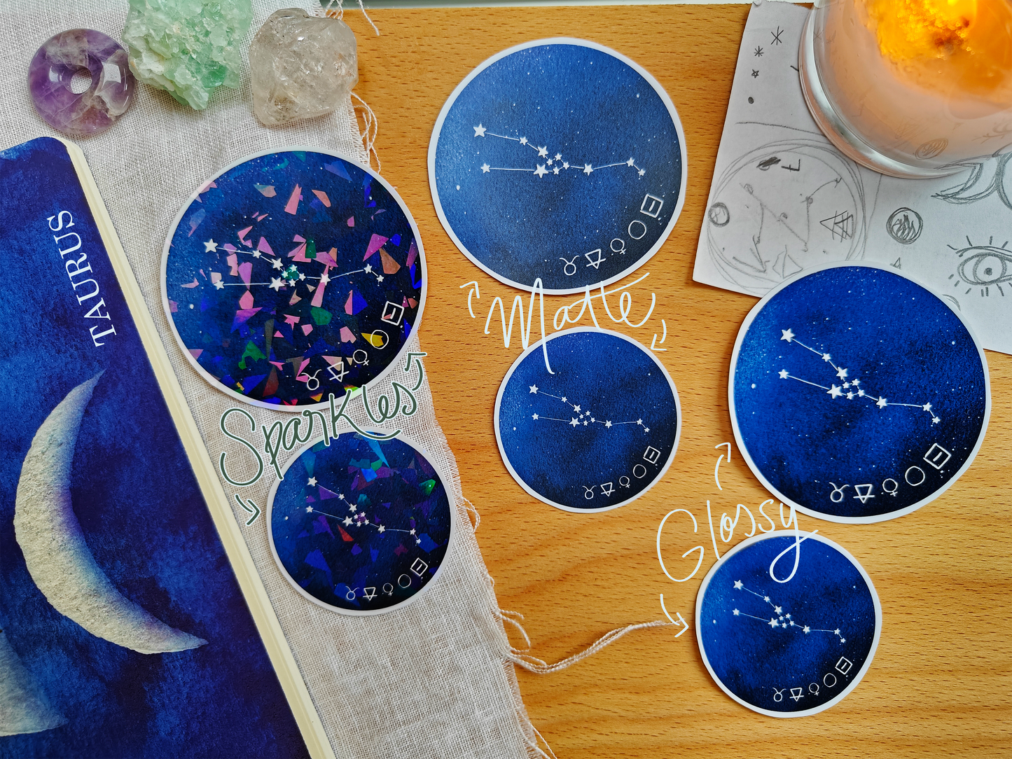 Set of blue astrological Constellation Stickers on a wooden surface with a candle, a journal, sketches, tarot cards and crystals.