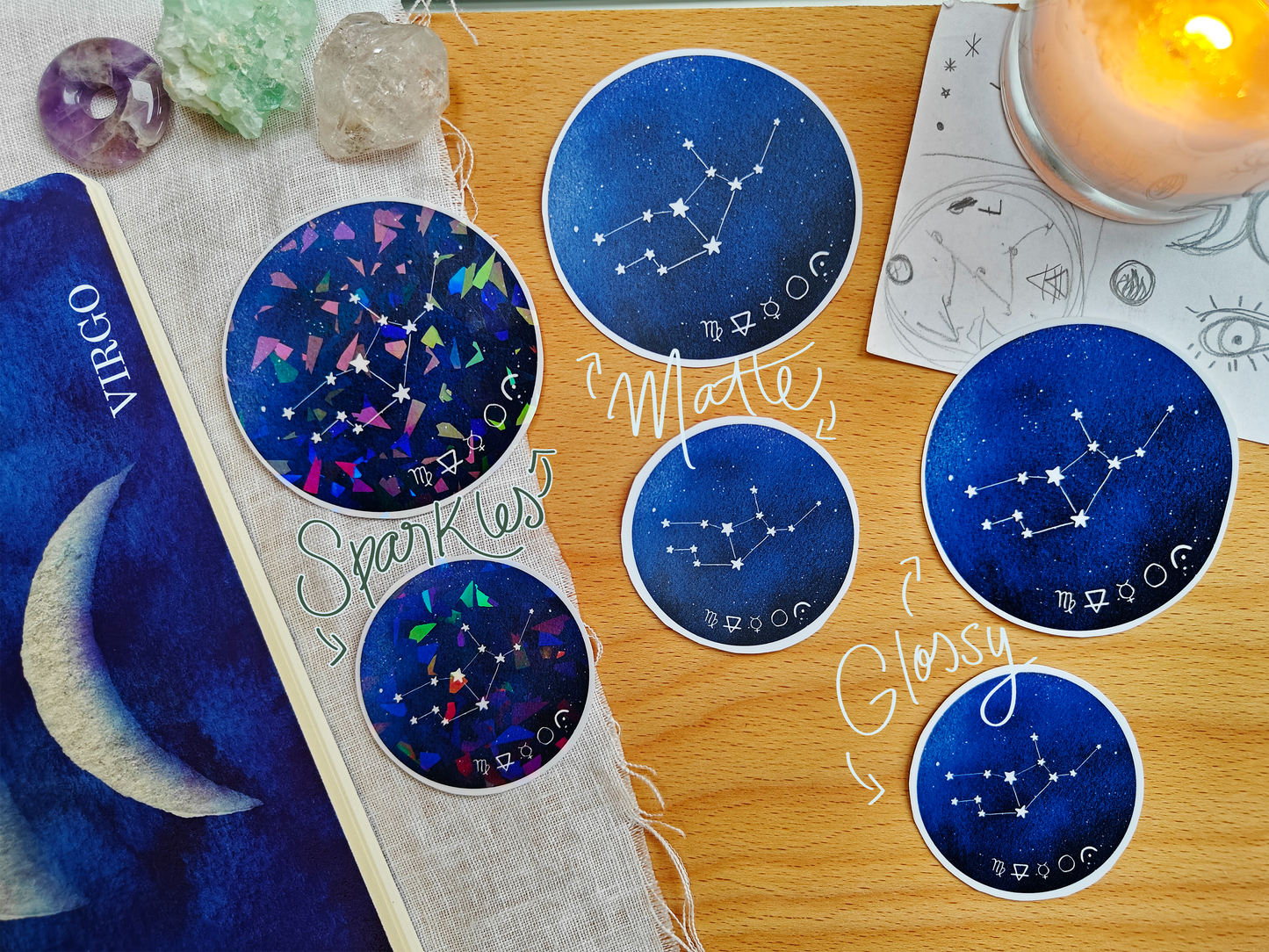 Set of blue astrological Constellation Stickers on a wooden surface with a candle, a journal, sketches, tarot cards and crystals.