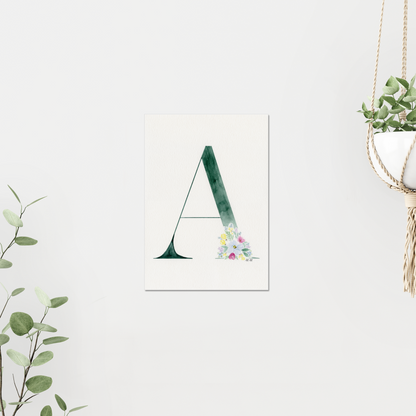 Decorative letter 'A' print with floral design on a white wall, surrounded by greenery. Made with watercolour.