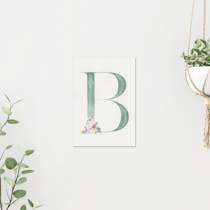 Letter 'B' print with floral design on a white wall, surrounded by greenery. Made with watercolours.